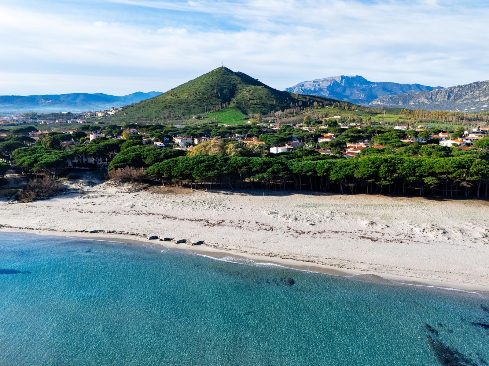 Beach with clear water, green hills and trees in the background.