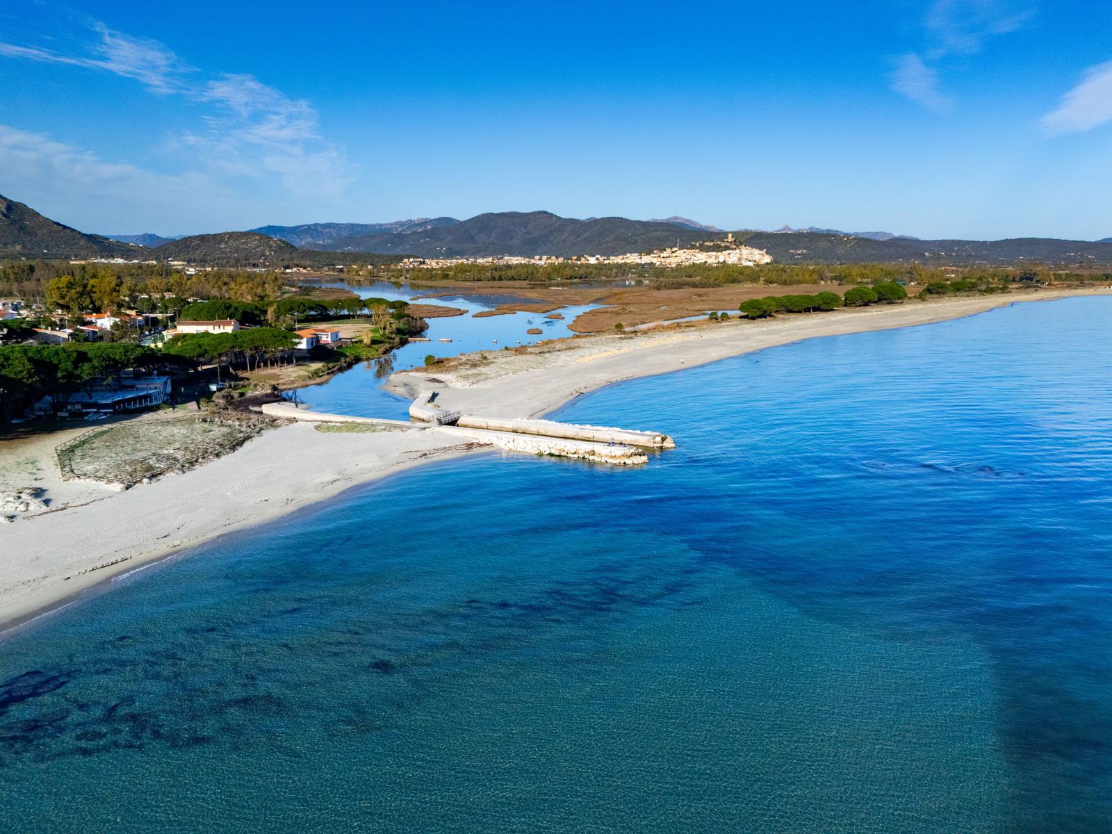 Beach with clear water, river, and hills in the background.