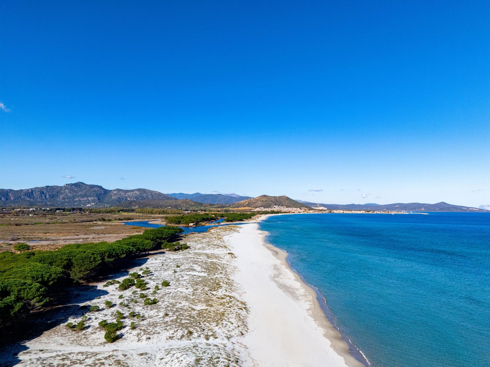 Beach with white sand, turquoise sea, and green trees along the coast.