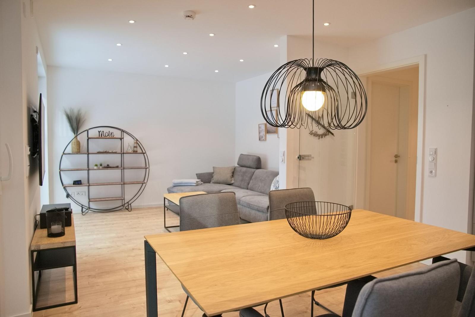 Essbereich mit Holztisch und Stühlen. Wohnbereich mit Sofa und runden Regal.