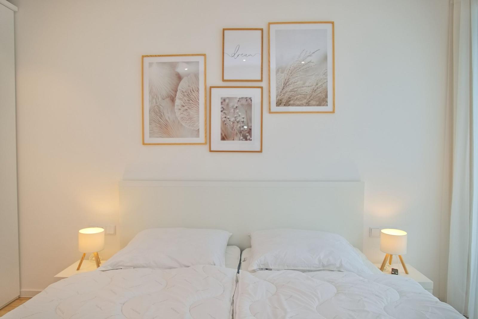 Ein Bett mit weißen Kissen und Decken, zwei Nachttische mit Lampen und Wanddekoration.