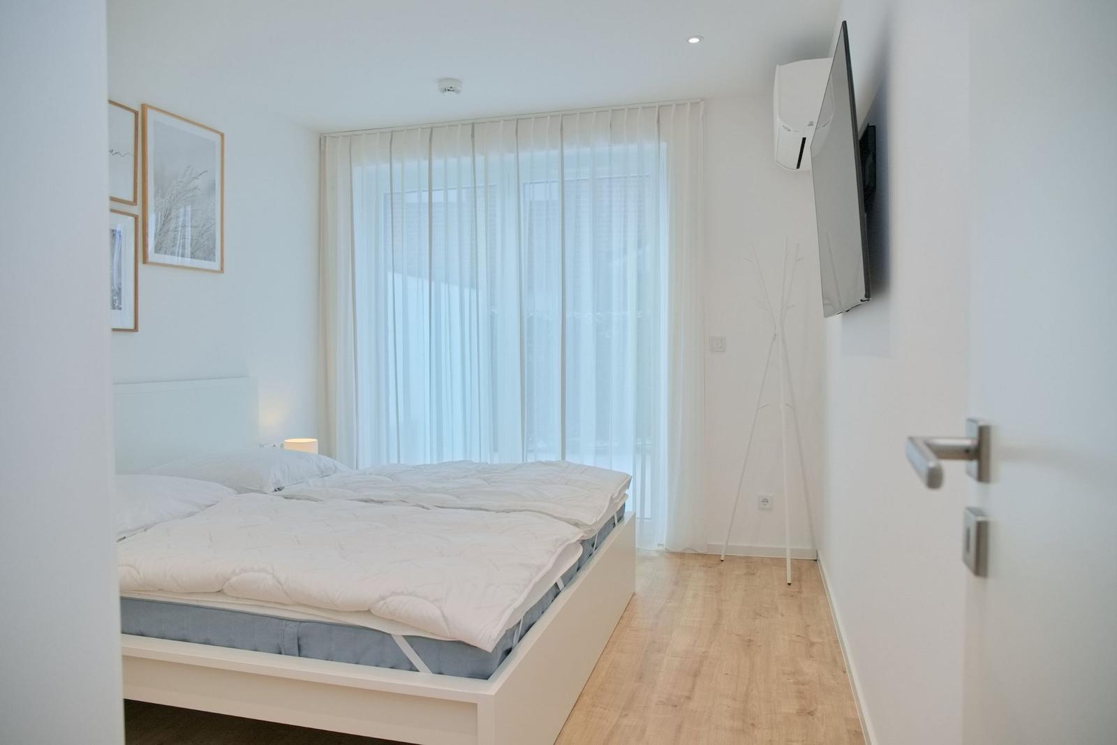 Schlafzimmer mit Bett, TV und Fenster mit Vorhängen.