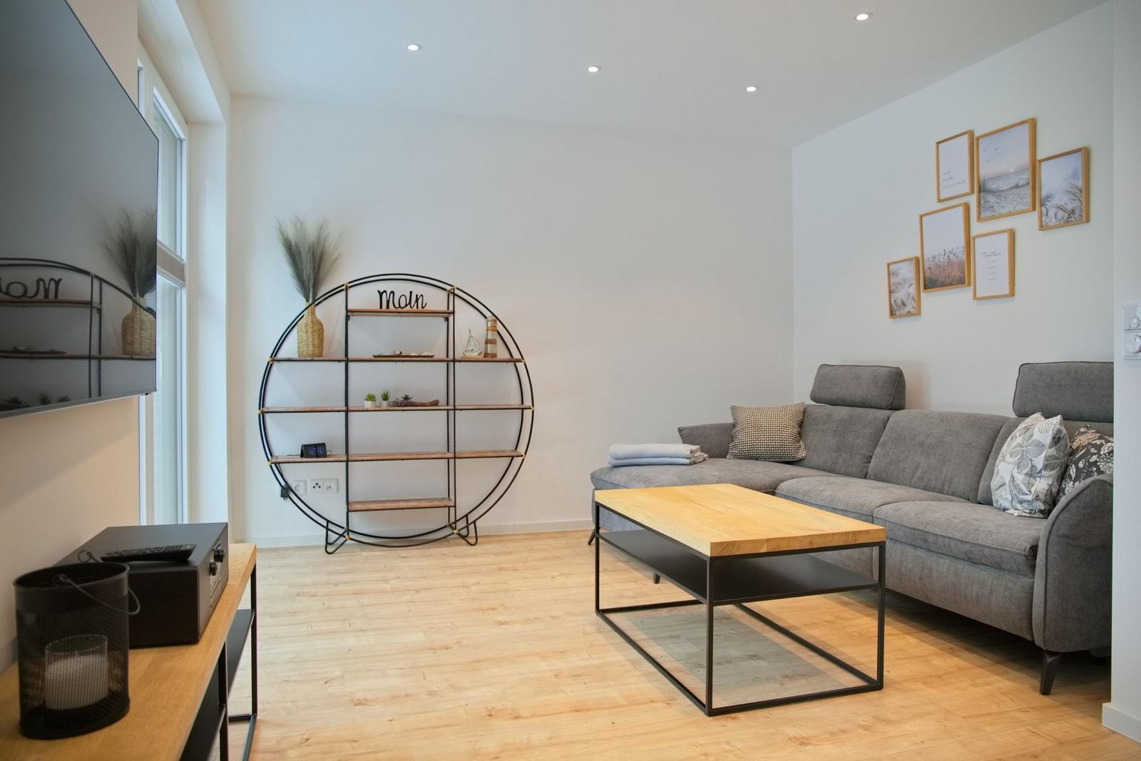 Wohnzimmer mit grauem Sofa, Holztisch und runden Regal.