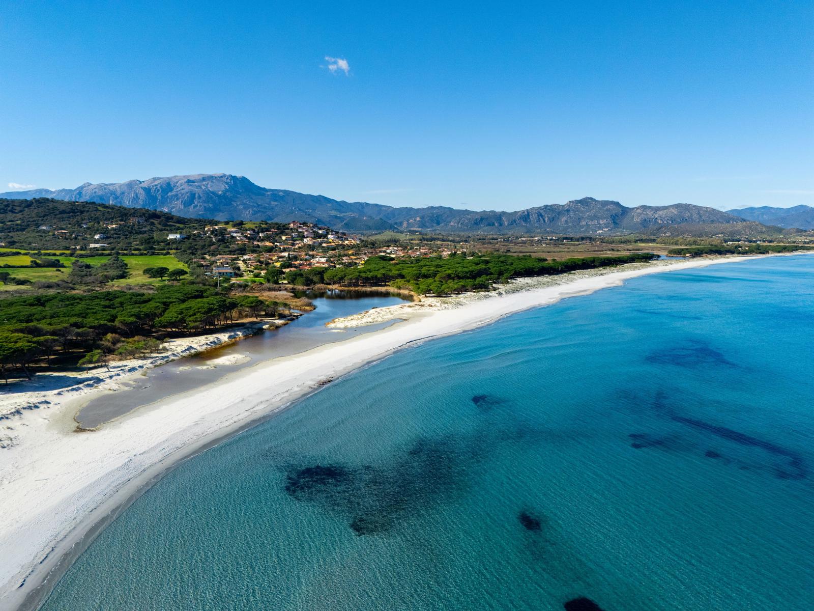 Strand mit kristallklarem Wasser und grüner Landschaft im Hintergrund.