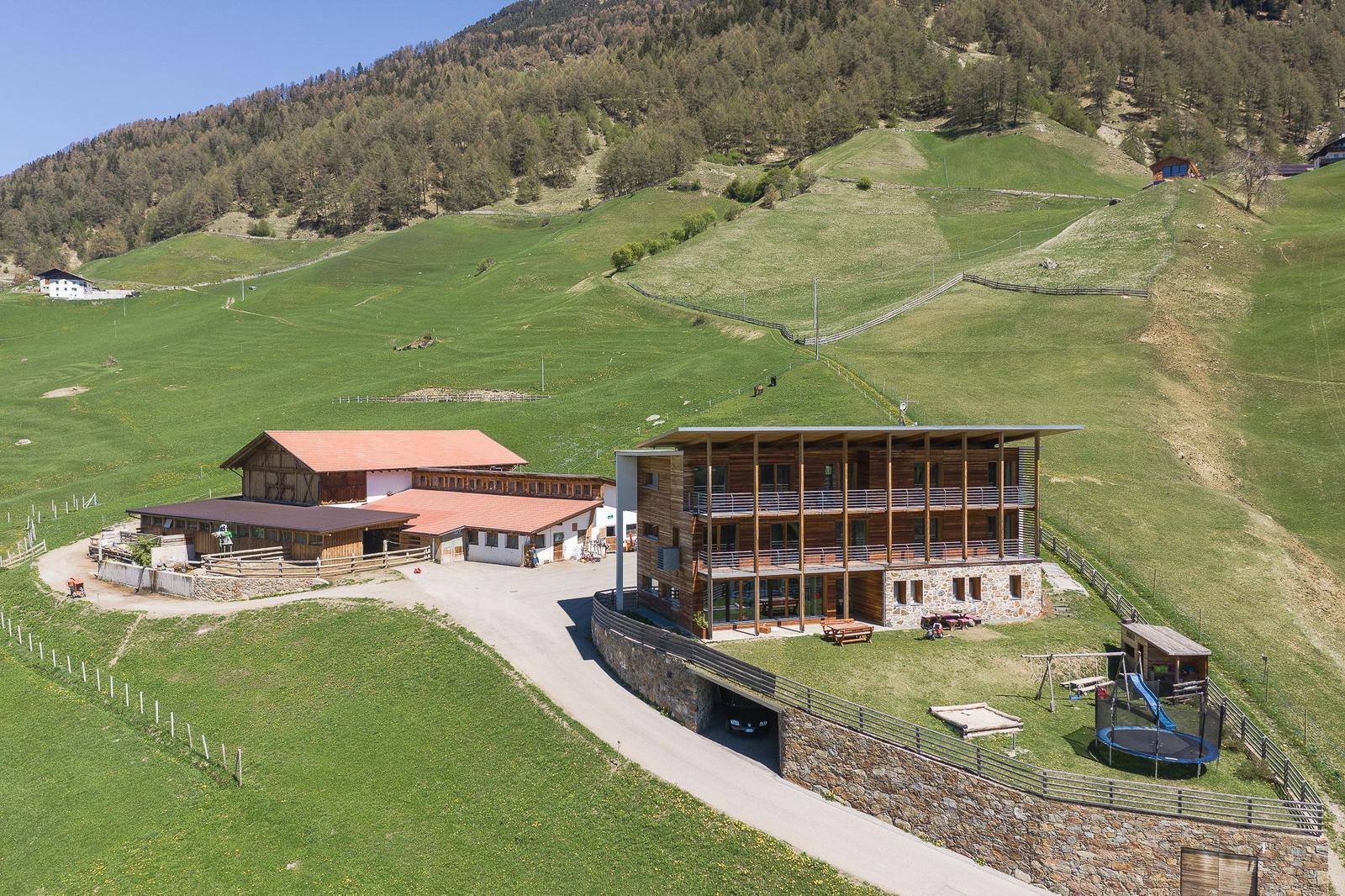 Modernes Holzhaus mit Terrasse, Spielplatz und Garage in grüner Berglandschaft.