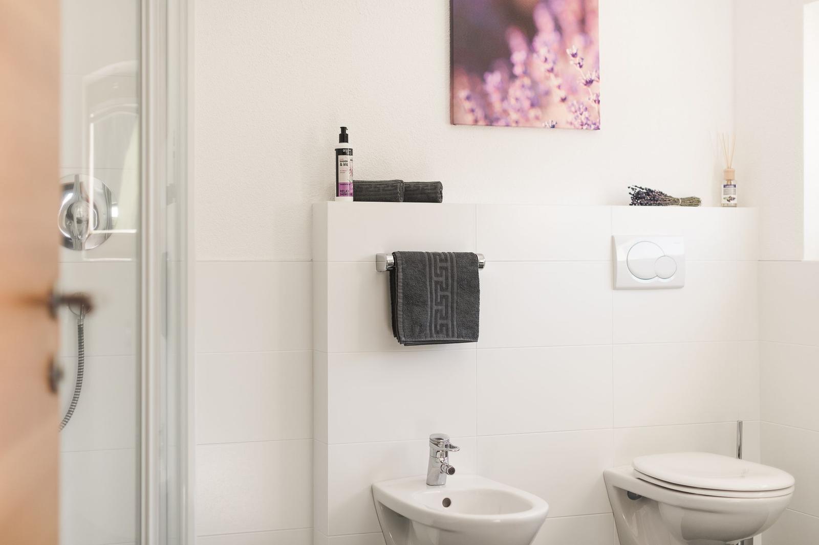 Badezimmer mit Dusche, Bidet und Toilette. Wandbild mit Lavendel.