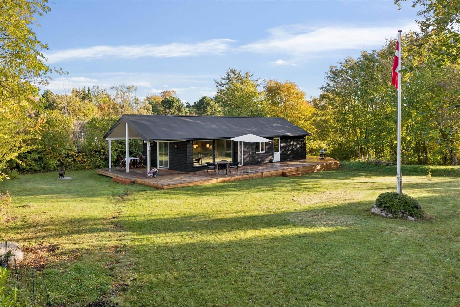Modern wooden cabin with terrace, garden, and Danish flag.