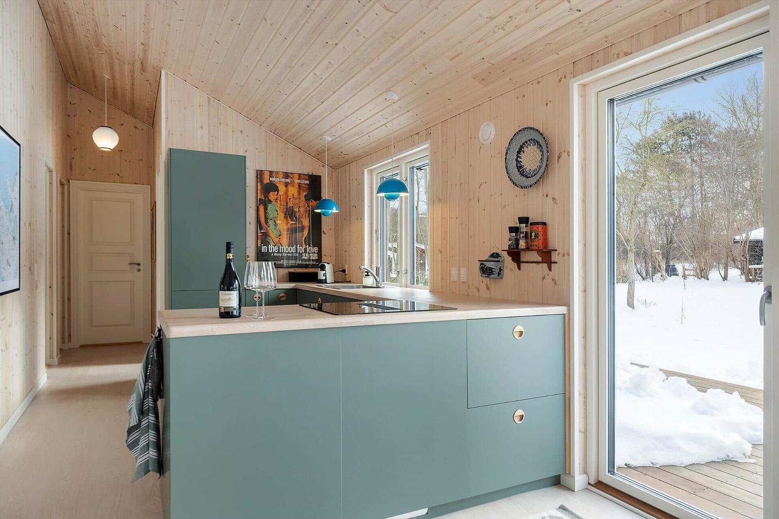 Kitchen with wooden walls and ceiling, blue countertop, and snowy view.