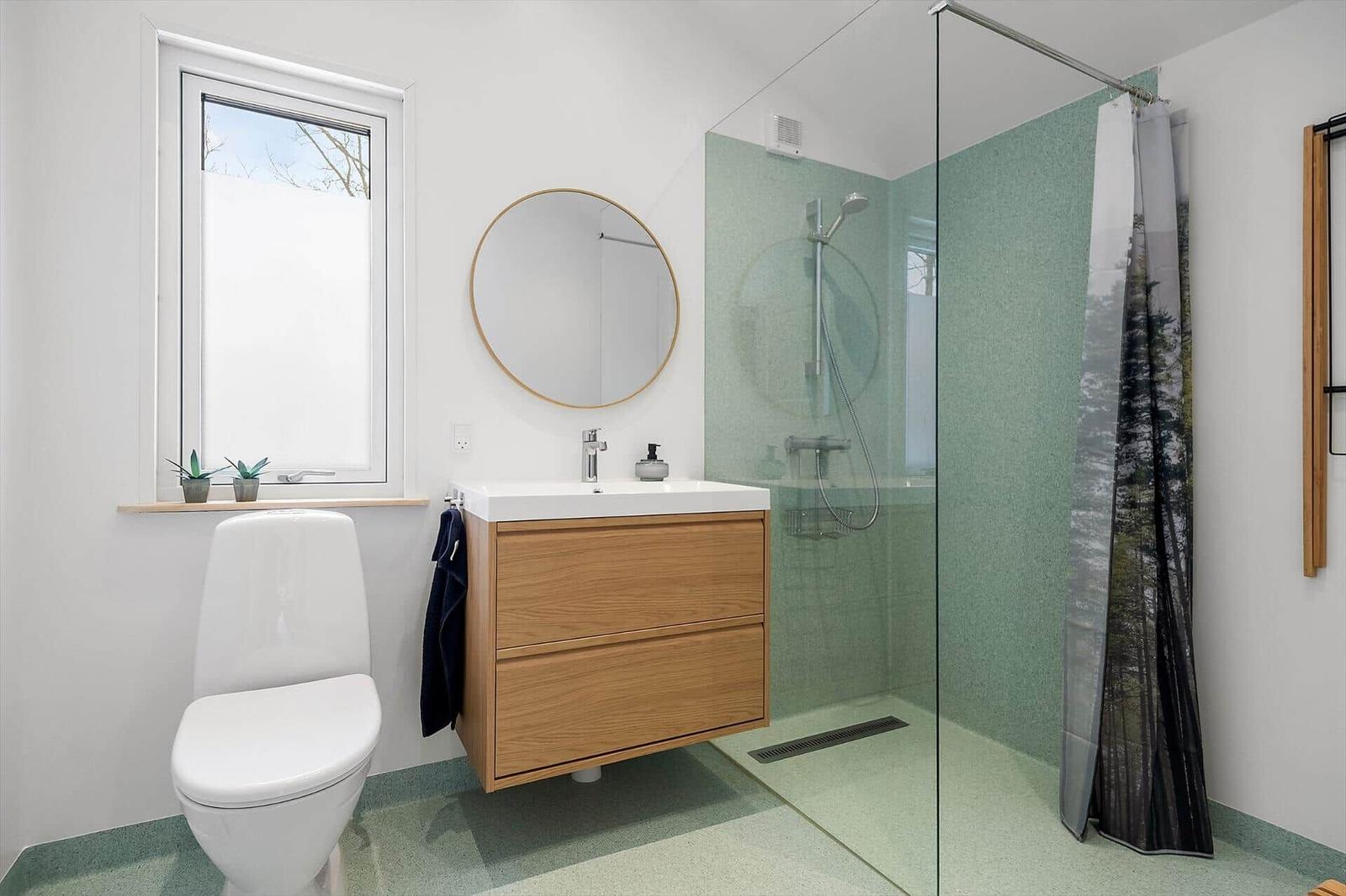 Bathroom with shower, sink, and toilet. Green tiles and wooden vanity.