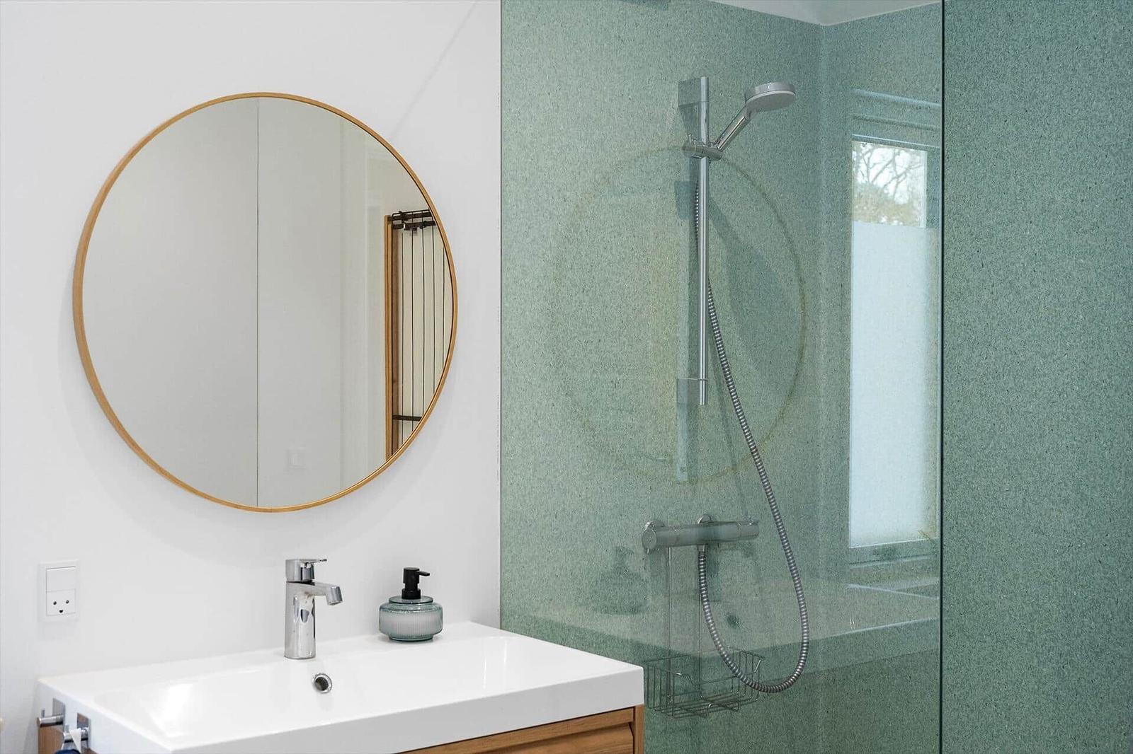 Bathroom with shower, sink, and round mirror.