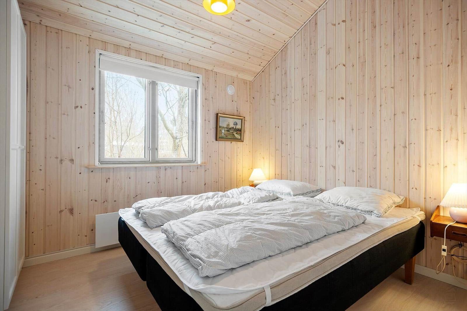Bedroom with wooden walls, bed, and window with view of trees.