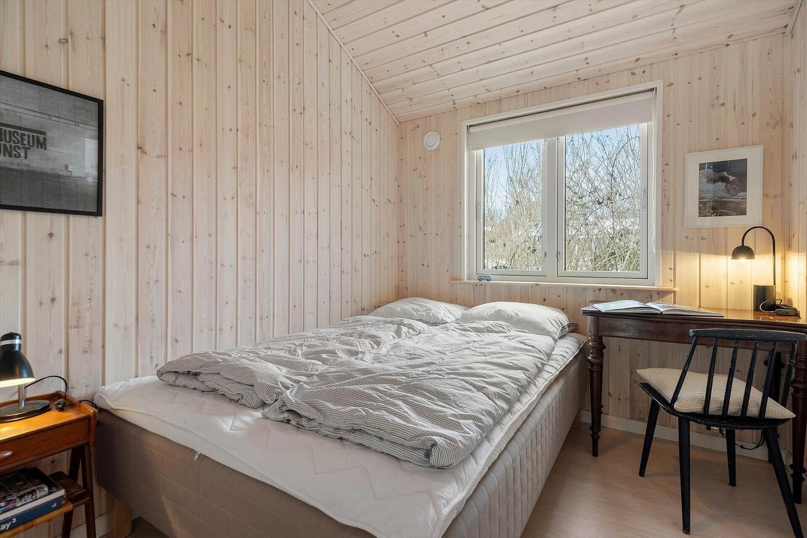Bedroom with wooden walls, bed, desk, and window.