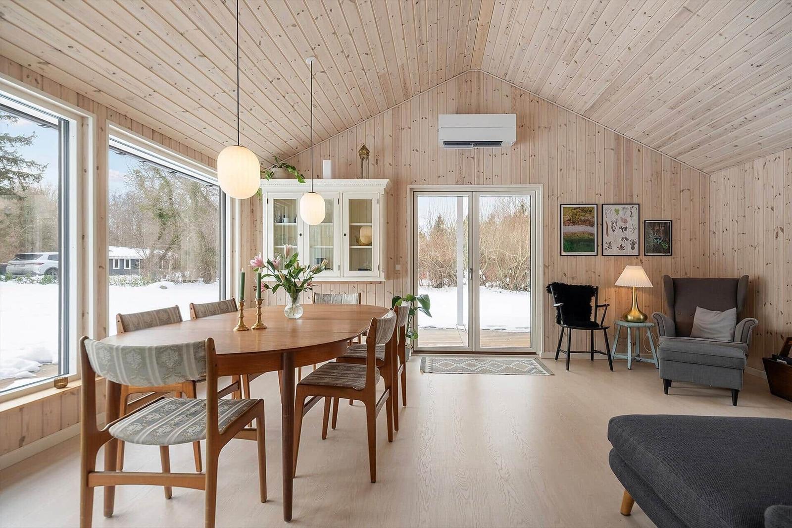 Dining room with wooden ceiling, table and chairs, windows and glass door to outdoor terrace.