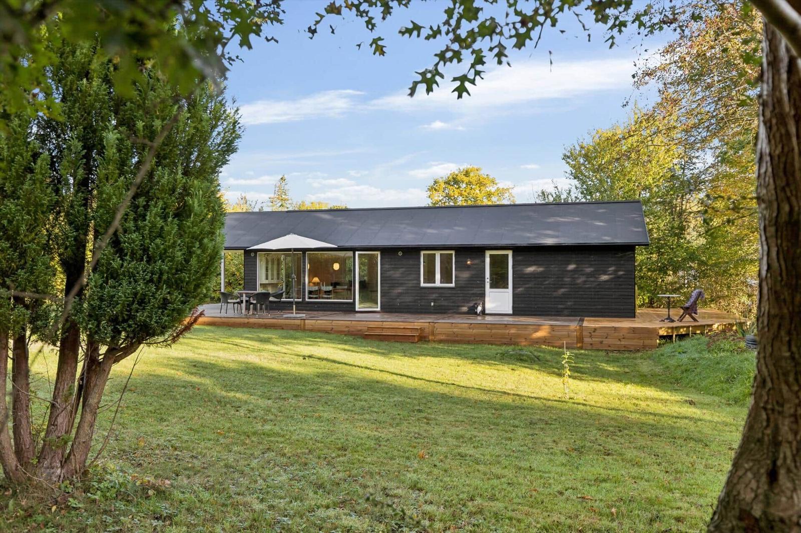 Modern black cabin with wooden terrace and garden. View through large windows.