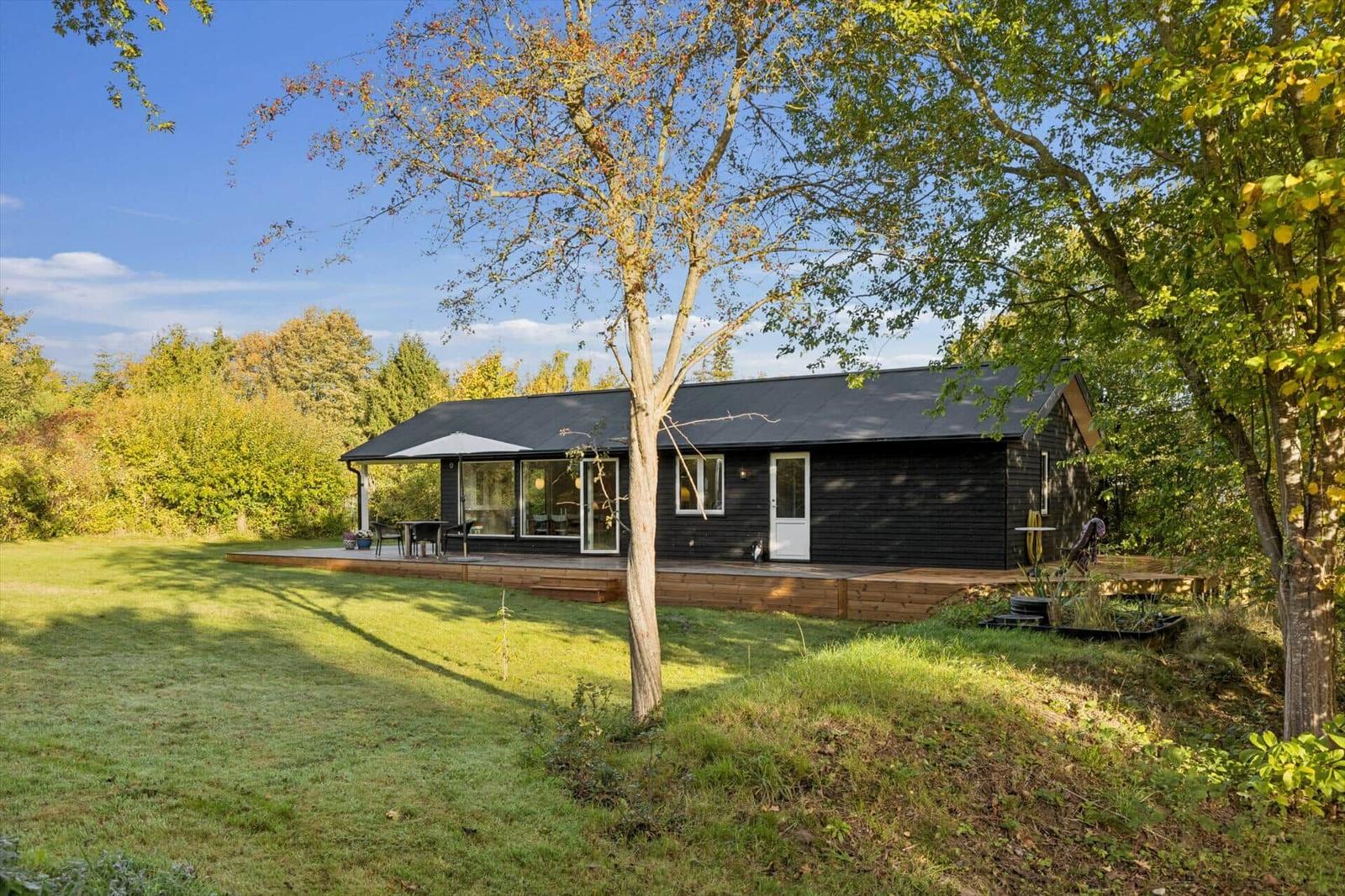 Black house with terrace and garden under trees.