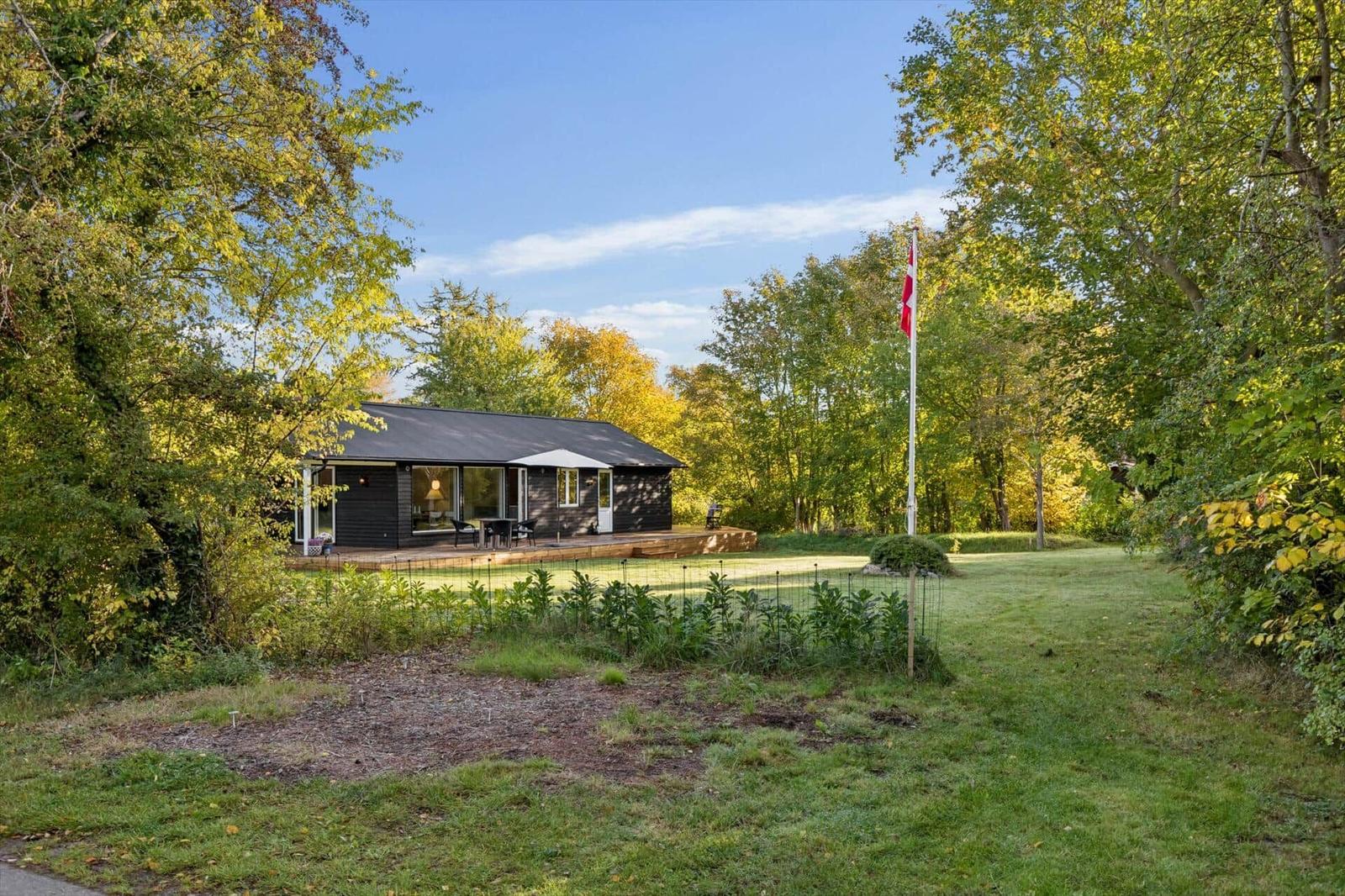 A modern house with a terrace, surrounded by grass and trees. A Danish flag flies.