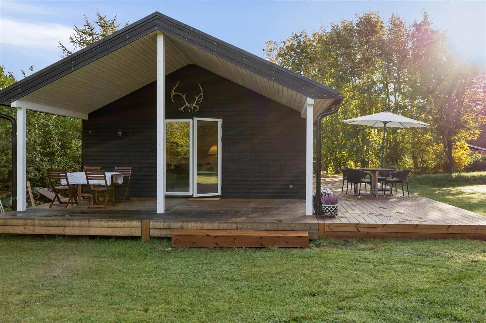 Wooden cabin with deck and garden. Table and chairs under umbrella.