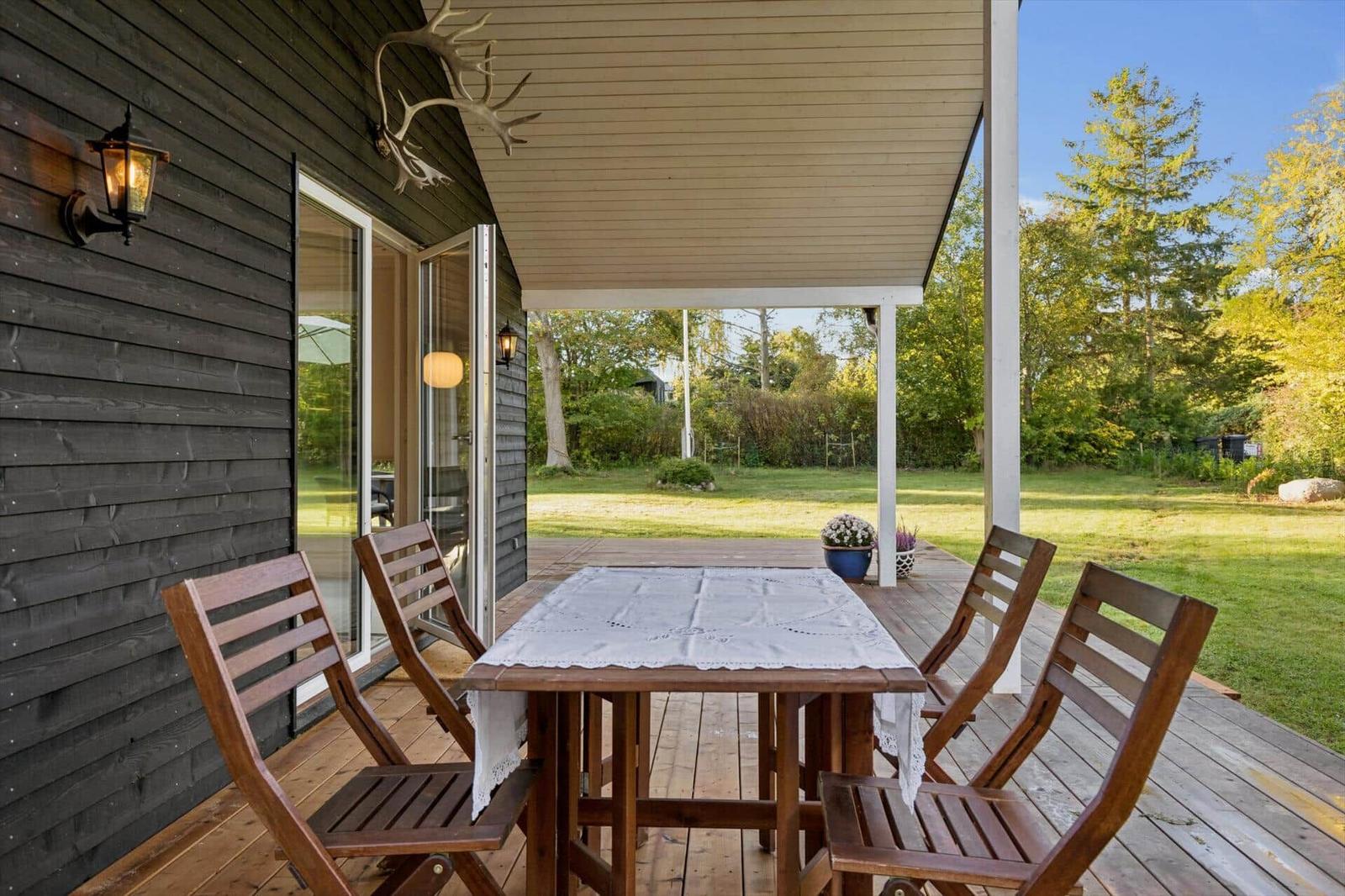 Deck with table and chairs, view of lawn and forest.