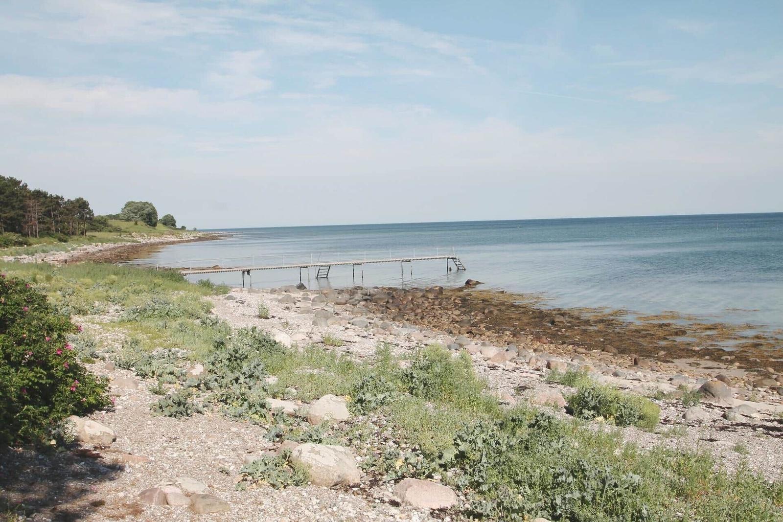 A pier leads to the sea. Shore with stones and grass. Sky with clouds.
