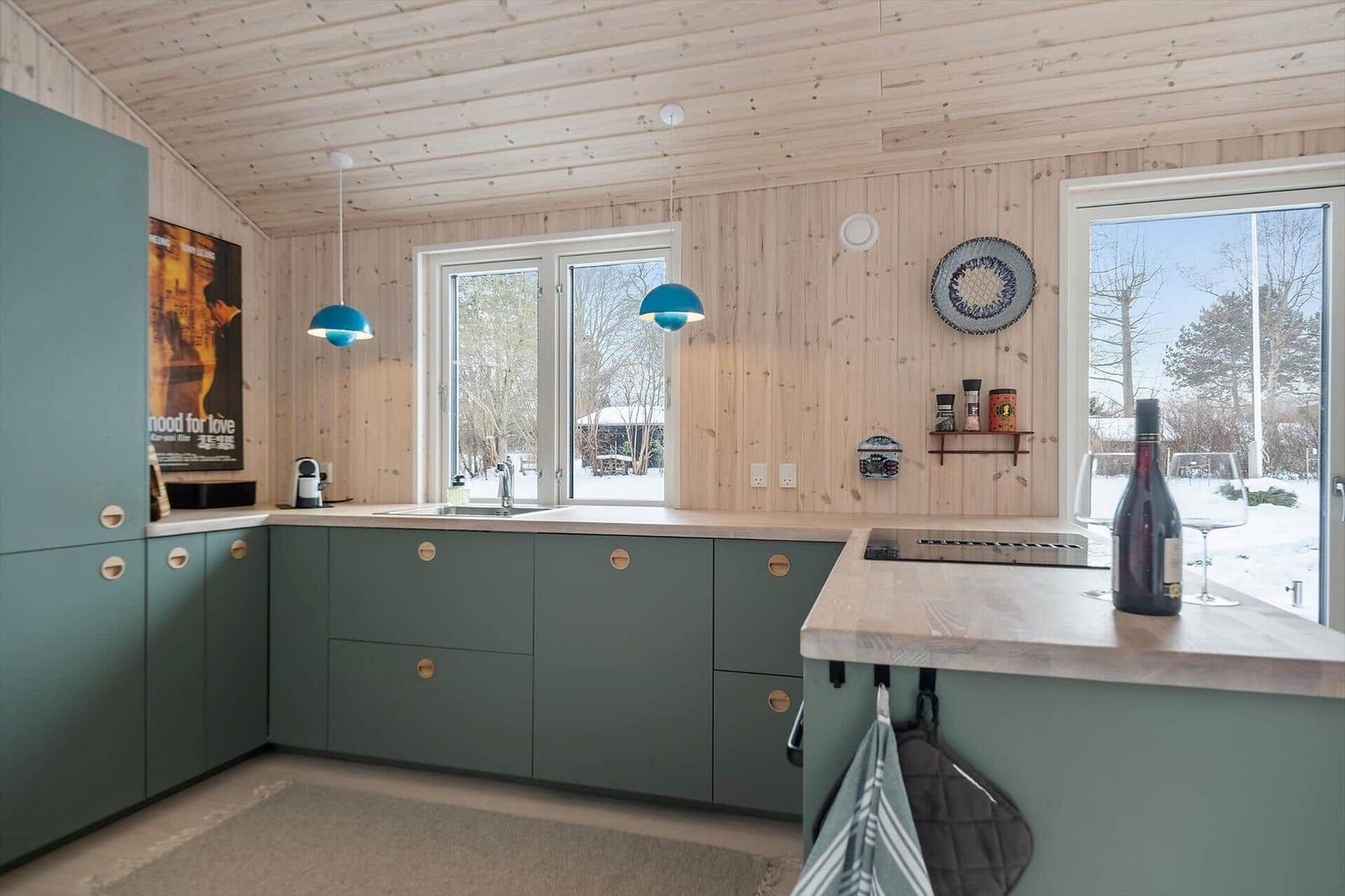 Kitchen with green cabinets, wooden walls, and windows to snow
