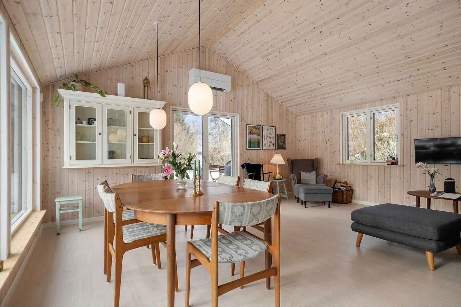 Dining room with wooden walls and dining table. Living area with sofa and TV.