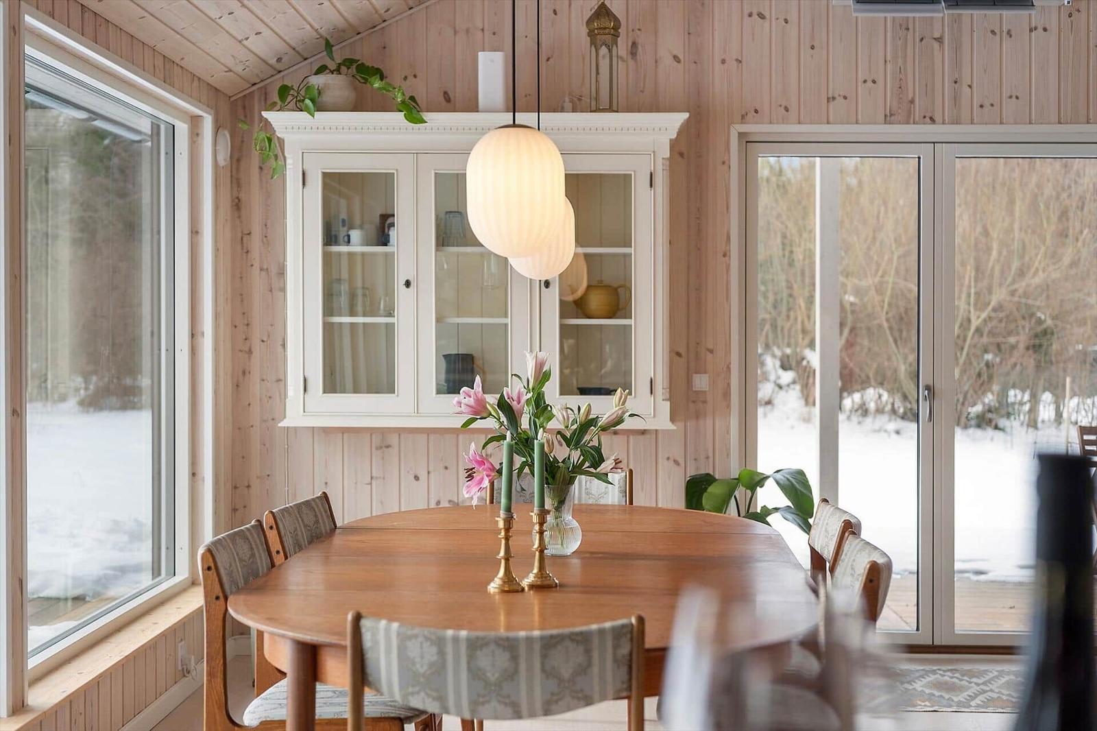 Dining room with wooden table, chairs, and glass doors. Windows show snow.
