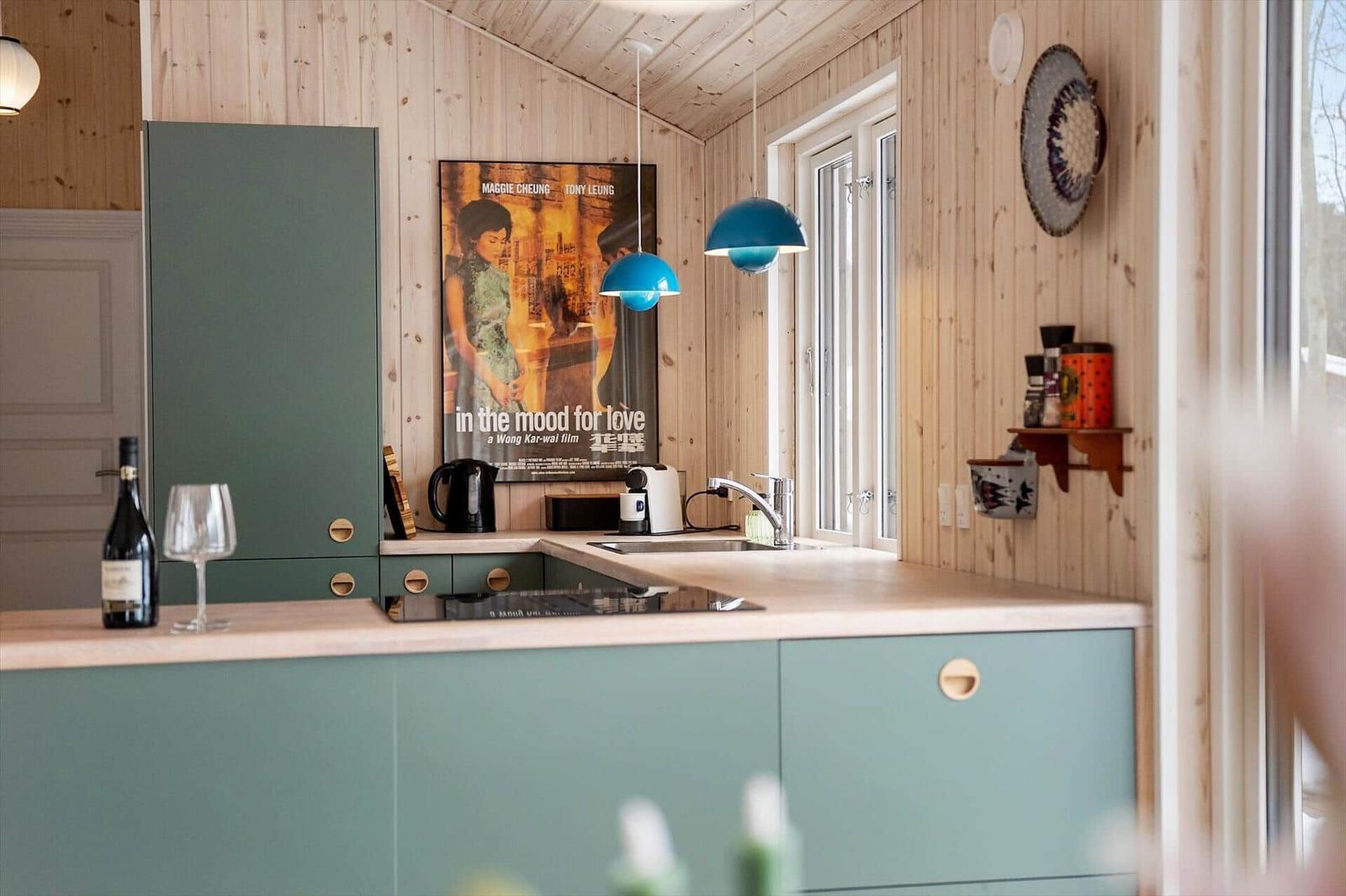 Kitchen with green cabinets, wooden walls, and blue pendant lights.