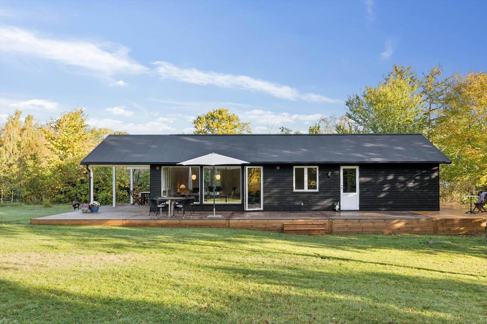 Black house with terrace, garden, and seating areas outdoors.