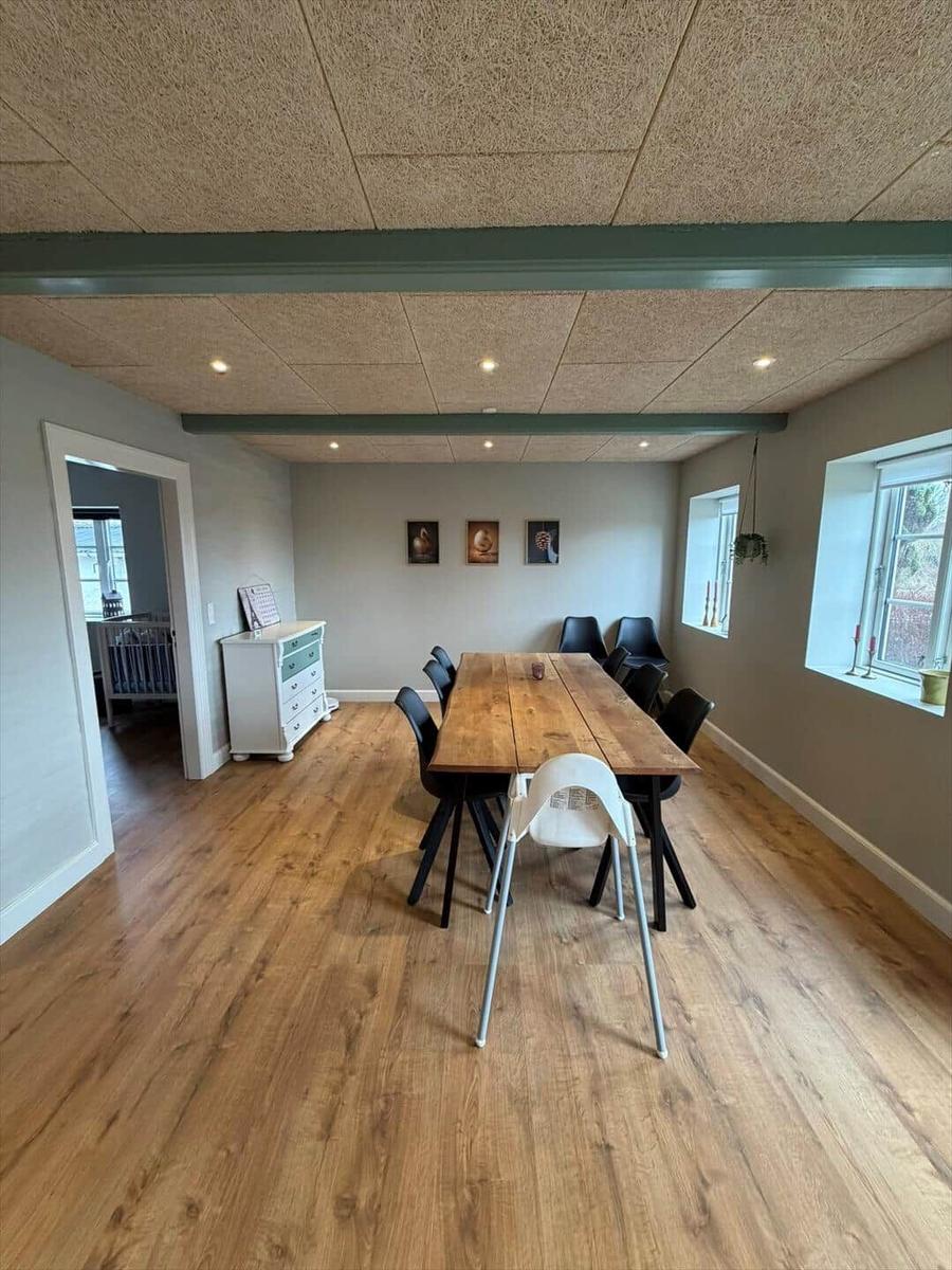 Dining room with wooden floor, long table and chairs. Windows and door visible.