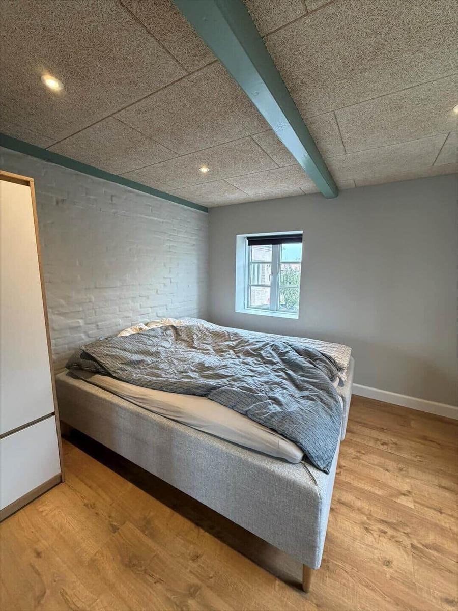 Bedroom with bed, wooden floor, and window. Ceiling with beams.