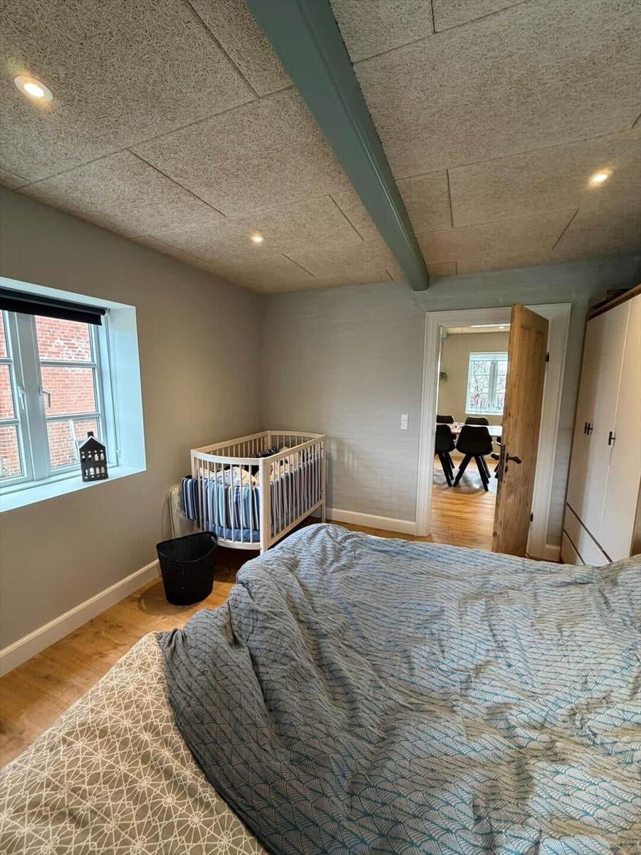 Bedroom with crib, bed, and window. Hallway to the kitchen.