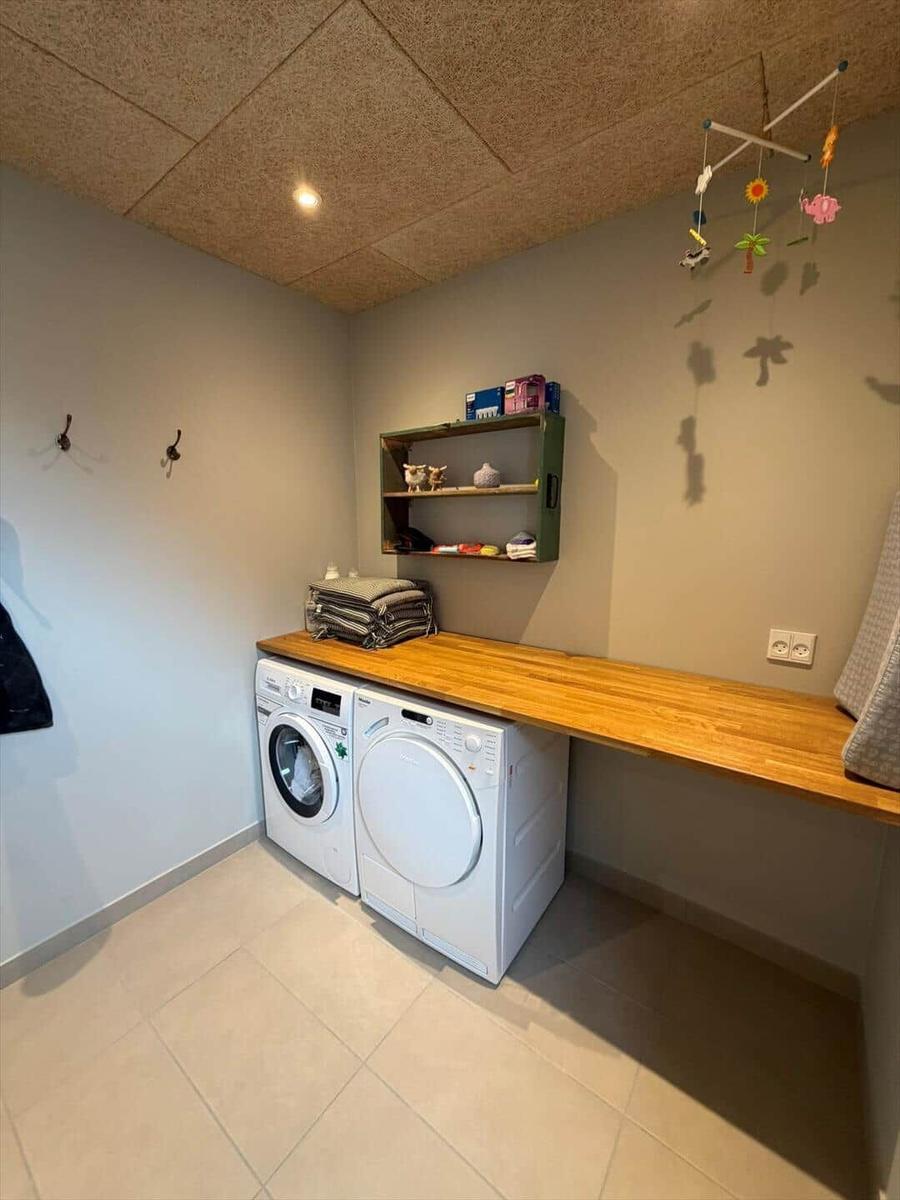 Laundry room with washing machine and dryer, wooden counter and wall shelf.