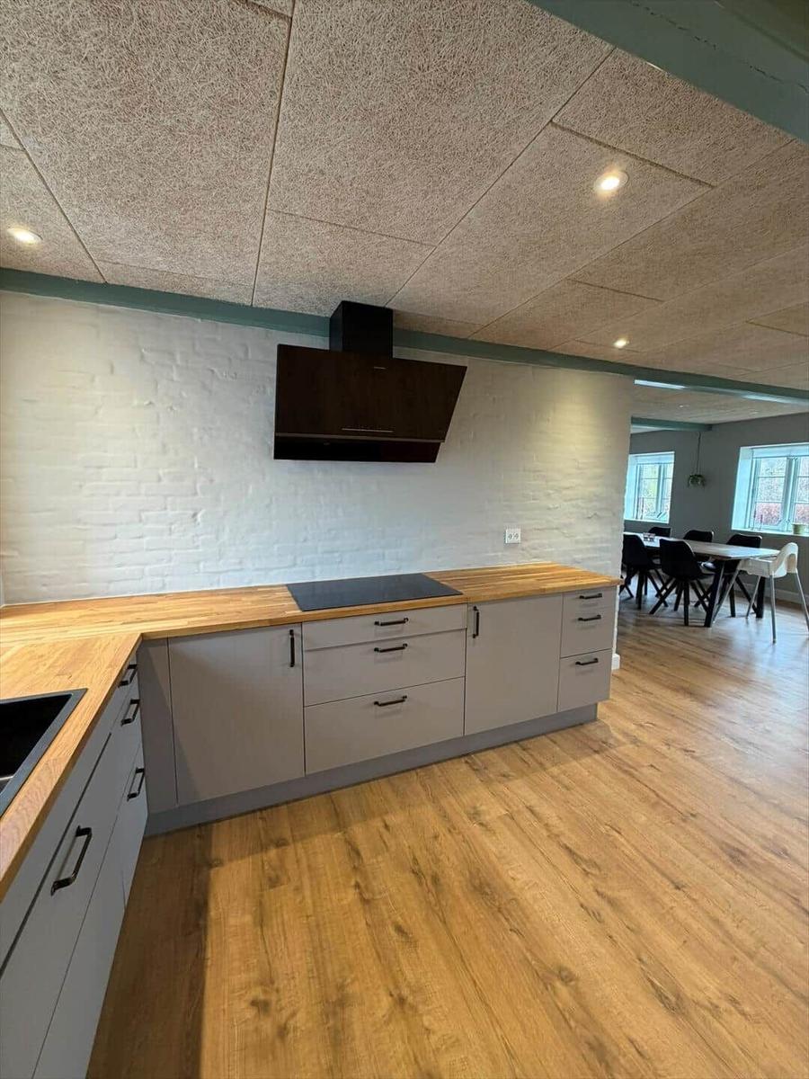 Kitchen with wooden surfaces and white wall. Dining area with table and chairs in background.