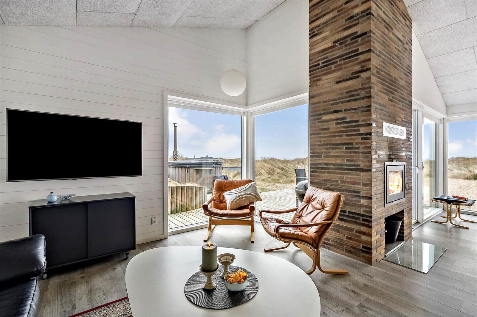 Wohnzimmer mit Kamin, TV und Blick auf Dünen.