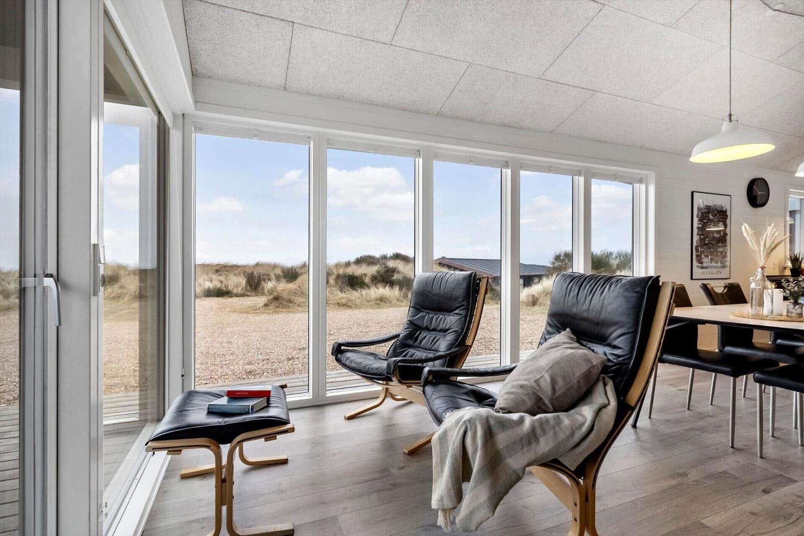 Zwei schwarze Ledersessel mit Holzrahmen stehen vor großen Fenstern mit Strandblick.