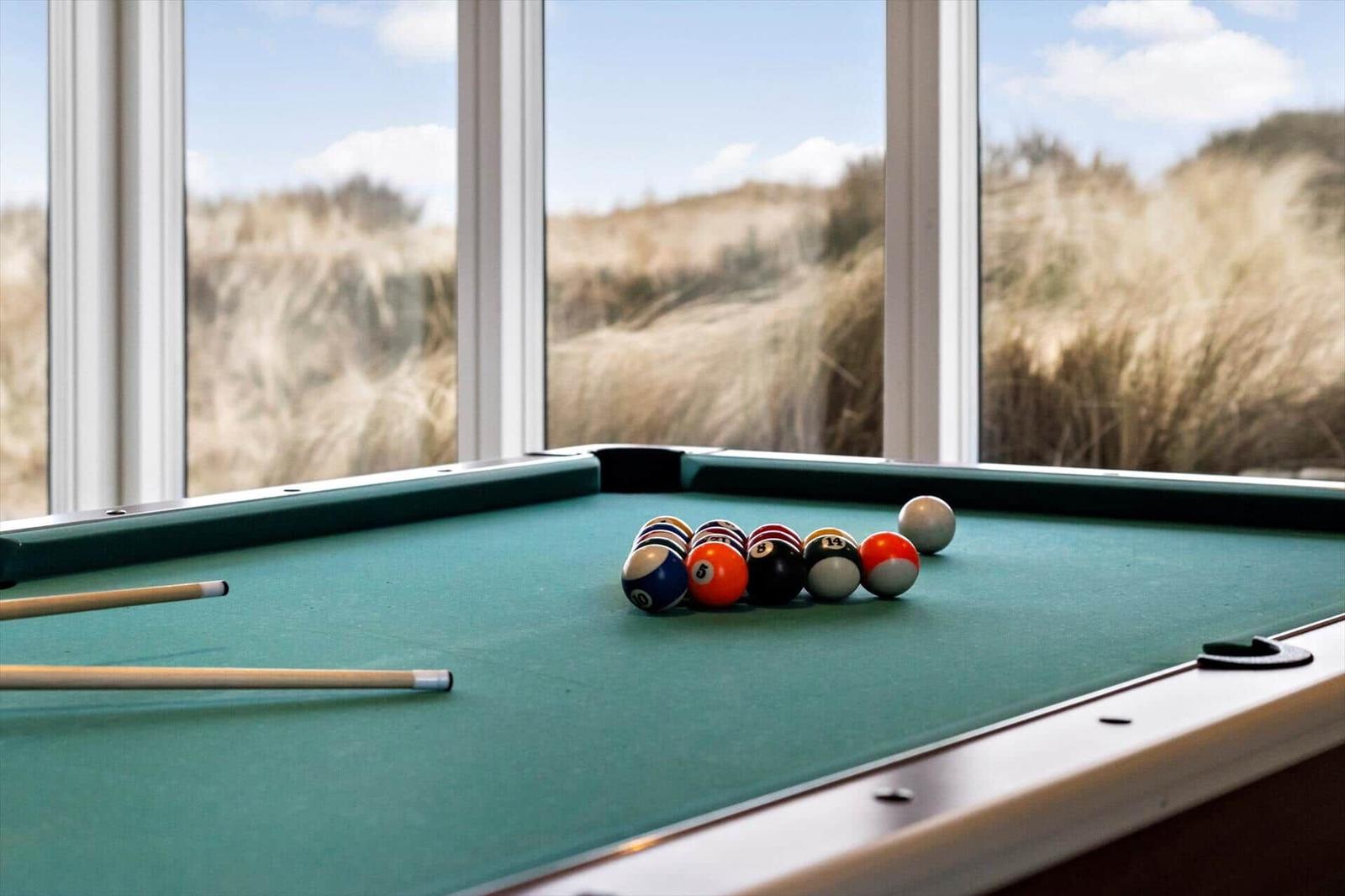 Billardtisch mit Kugeln vor großem Fenster mit Dünenblick
