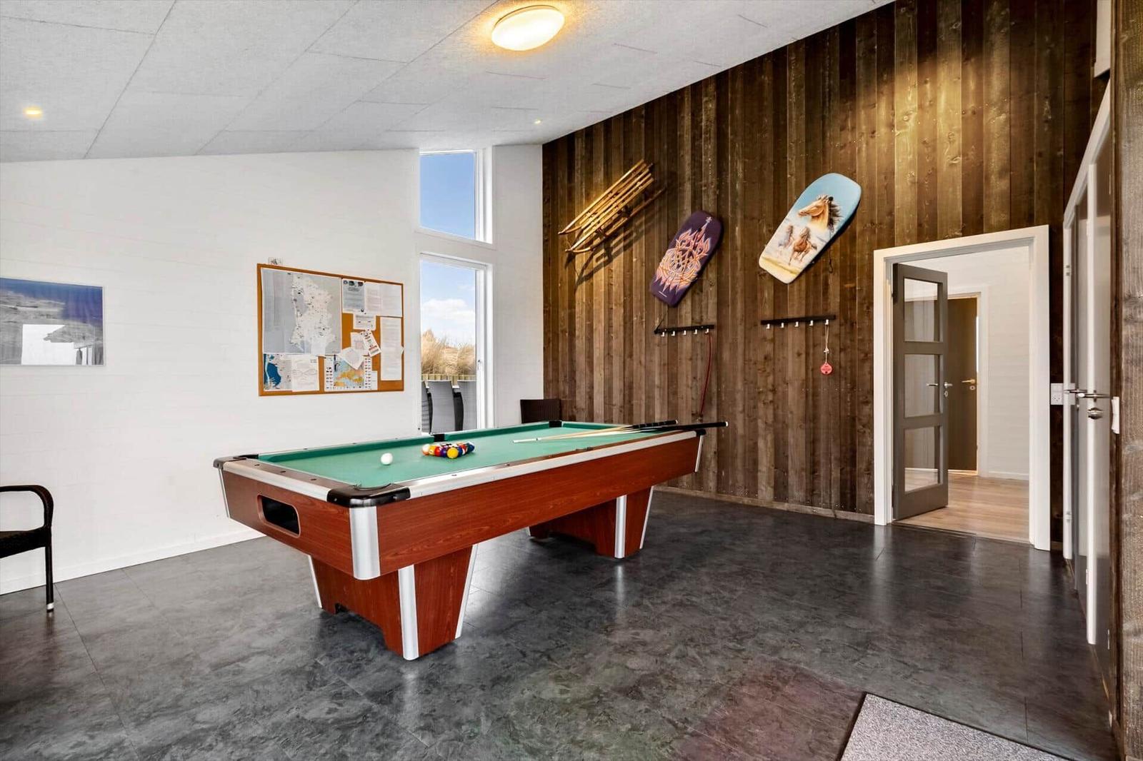 Billardtisch mit grünem Tuch und Kugeln in einem Raum mit Holzwand und Fenster.