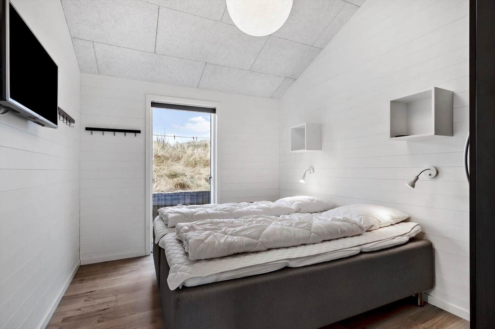 Schlafzimmer mit Bett, TV und Fensterblick auf Dünen.