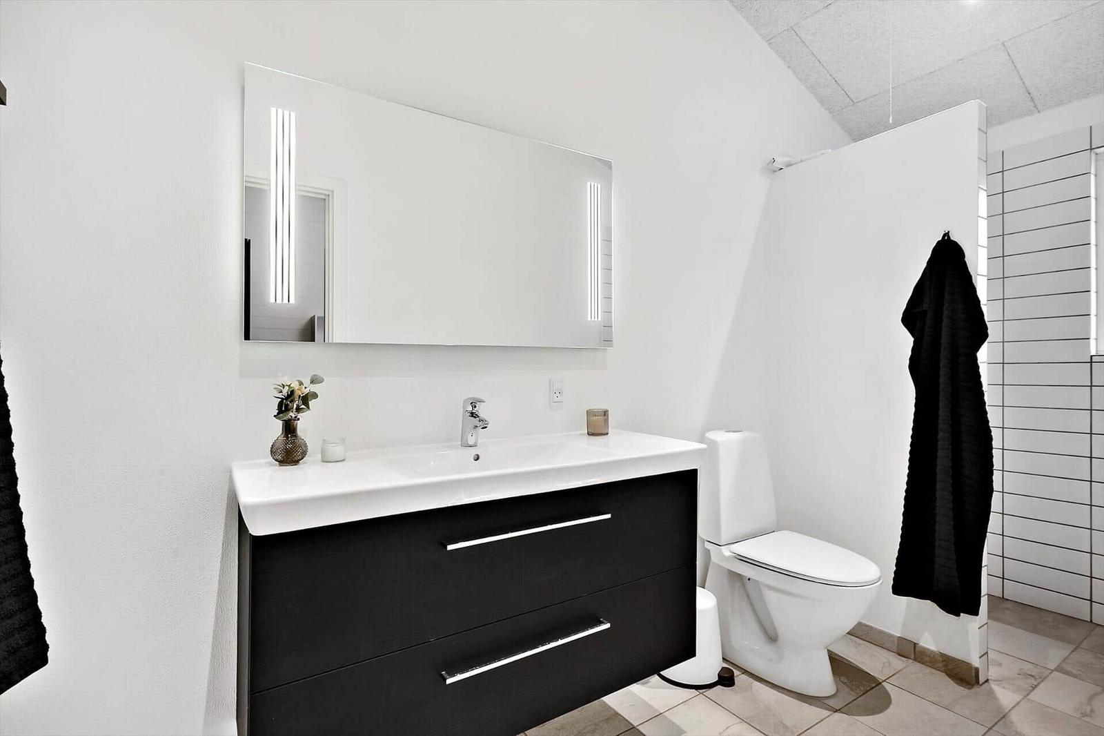 Badezimmer mit Waschtisch, Spiegel und Toilette. Schwarzer Schrank und schwarzes Handtuch.