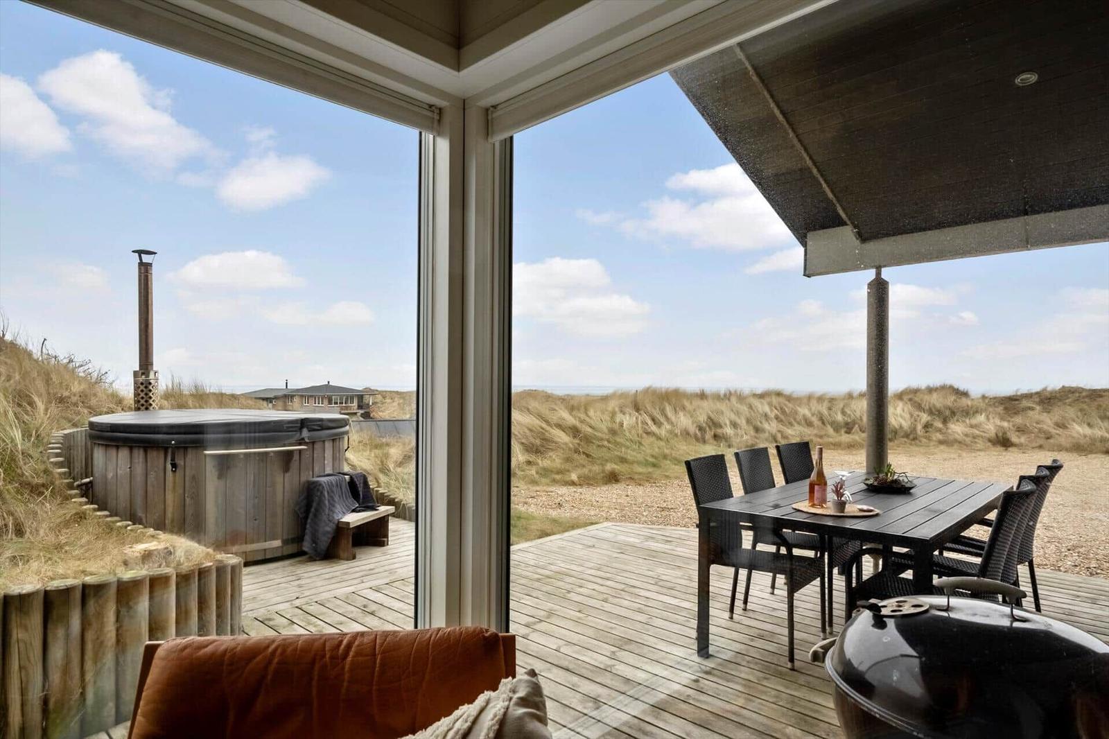 Terrasse mit Sitzgelegenheit, Esstisch und Whirlpool. Blick auf Dünen und Meer.