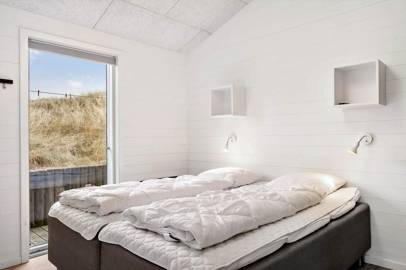 Schlafzimmer mit Doppelbett und Fensterblick auf Dünen.