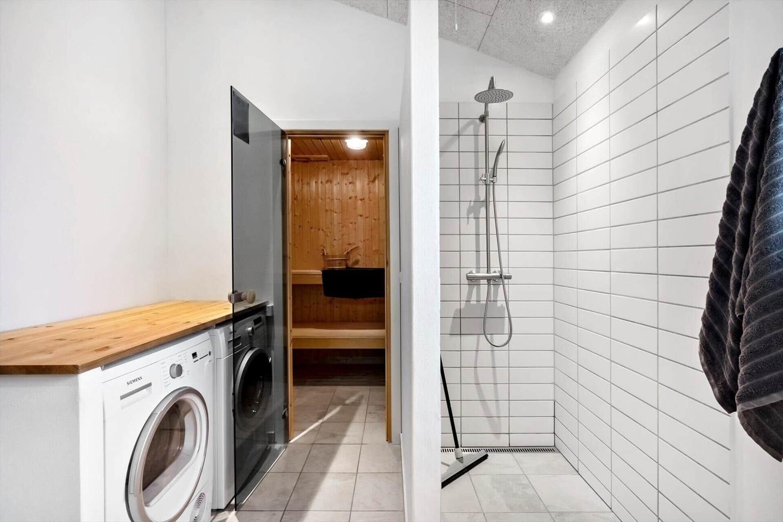Dusche mit Duschbrause, Waschmaschine und Sauna im Hintergrund.