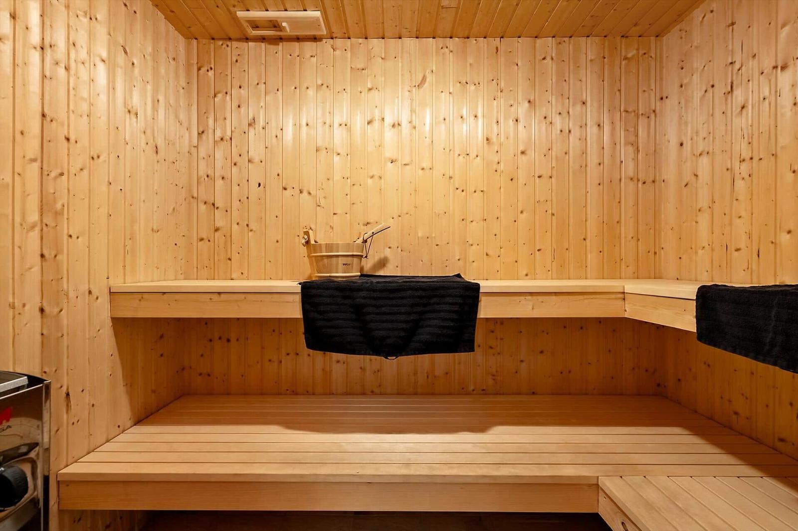 Sauna mit Holzbank und Eimer. Schwarze Handtücher hängen auf der Bank.
