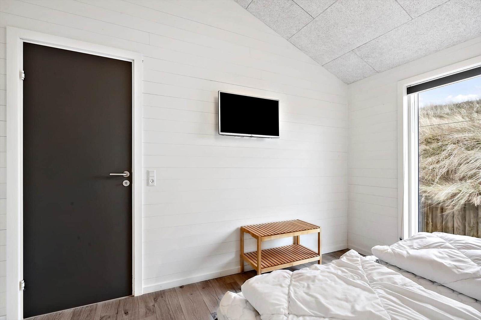 Schlafzimmer mit Bett, TV und Fensterblick auf Dünen.