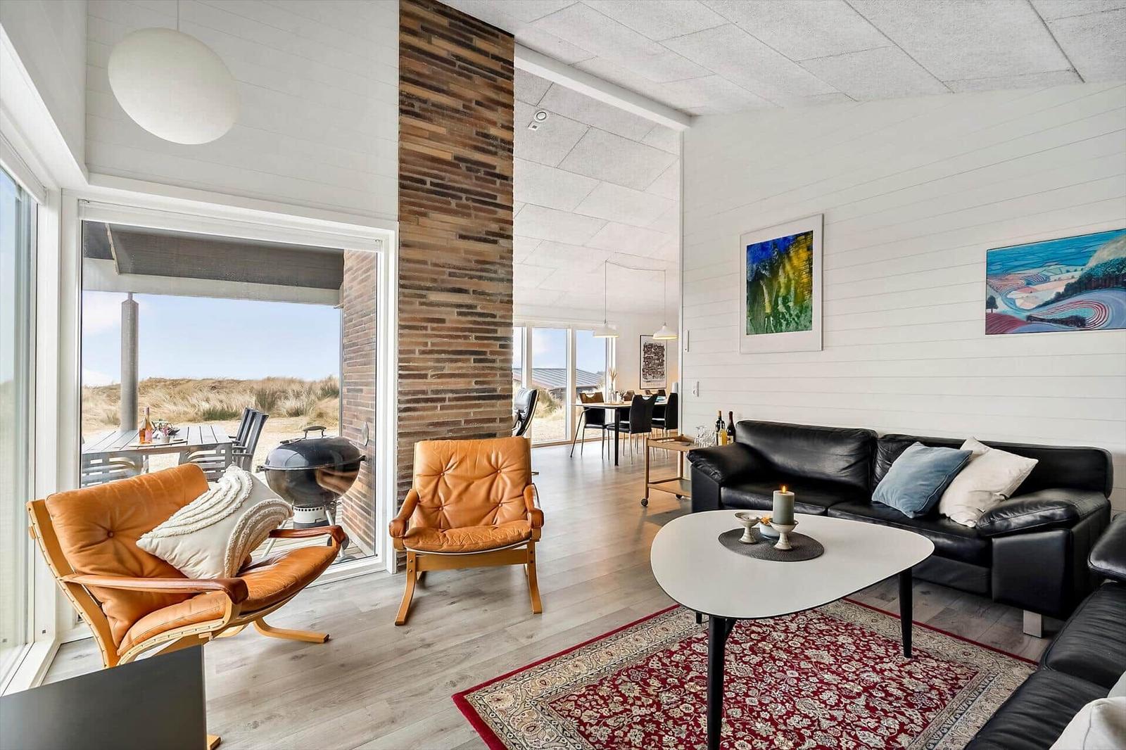 Wohnzimmer mit Ledersofa, zwei braunen Ledersessel und rotem Teppich.