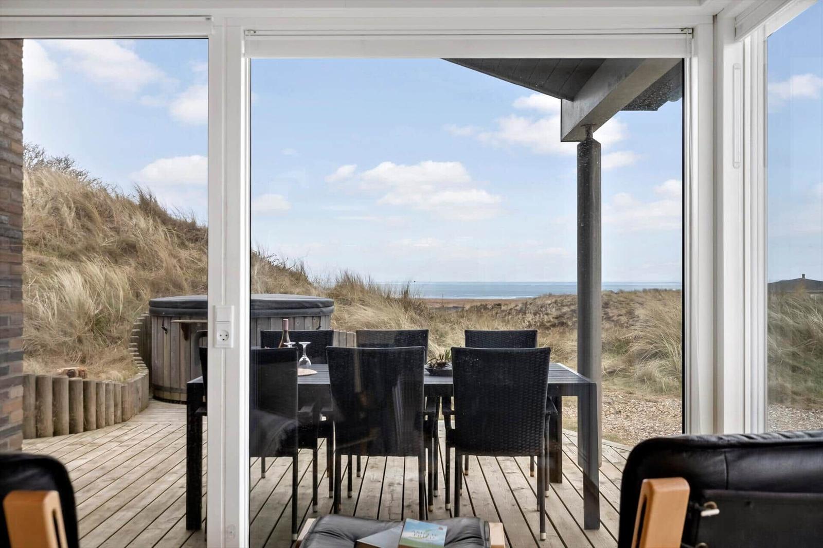 Terrasse mit Tisch und Stühlen, Blick auf Strand und Dünen.