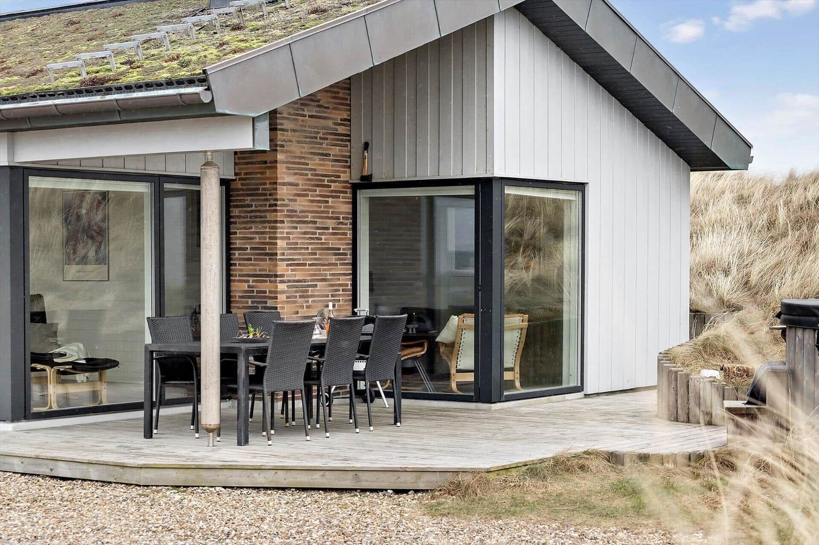 Haus mit Holzterrasse, Sitzgruppe und Glasfront zur Aussicht.