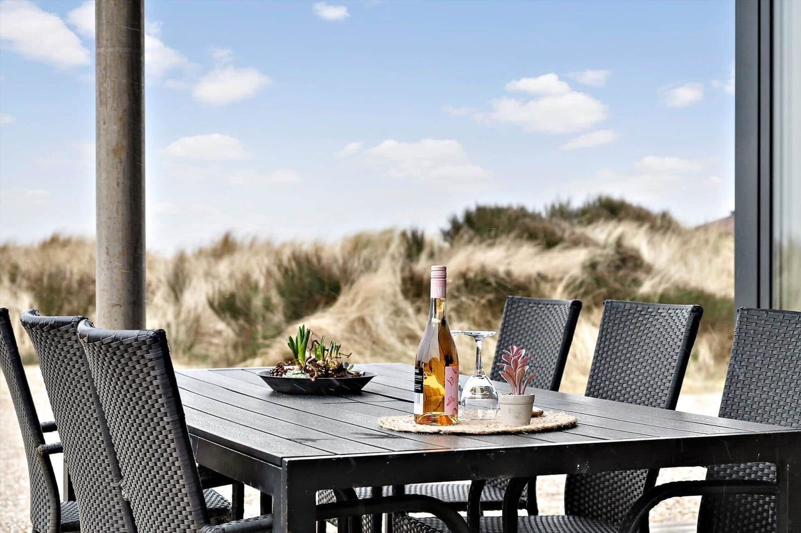 Terrasse mit Tisch und Stühlen, Blick auf Dünen und Himmel.