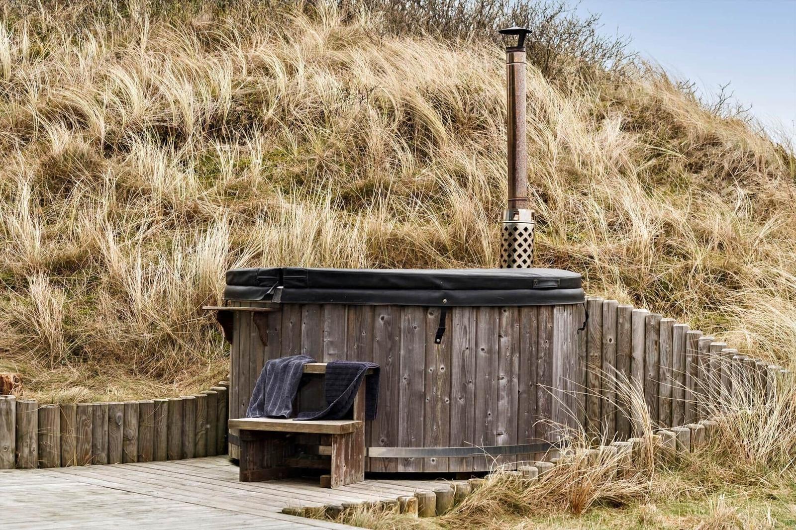 Holzwhirlpool mit Sitzbank und Schornstein auf Holzterrasse vor Grasberge