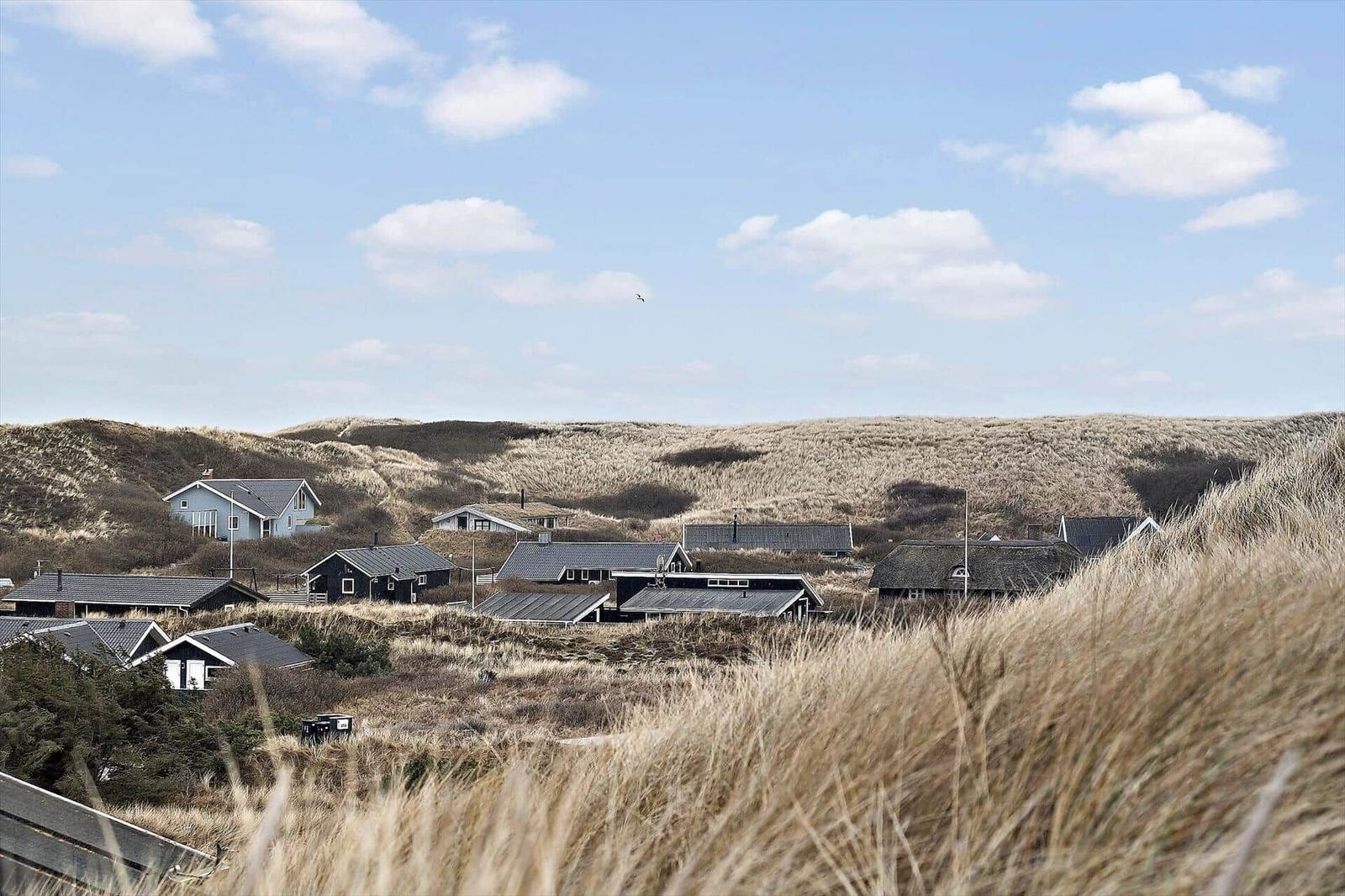 Dorf zwischen Dünen mit Häusern unter blauem Himmel.